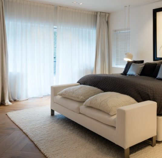 Luxe villa verbouwing – slaapkamer met linnen overgordijnen, wollen kleed, Flos verlichting en design bench
