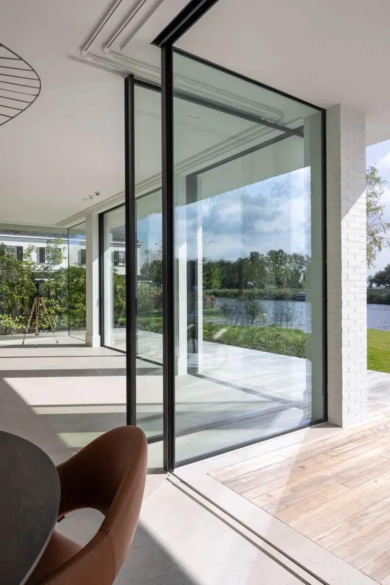 Moderne villa met glazen schuifpui en uitzicht op het water – interieur met naadloze overgang tussen binnen en buiten