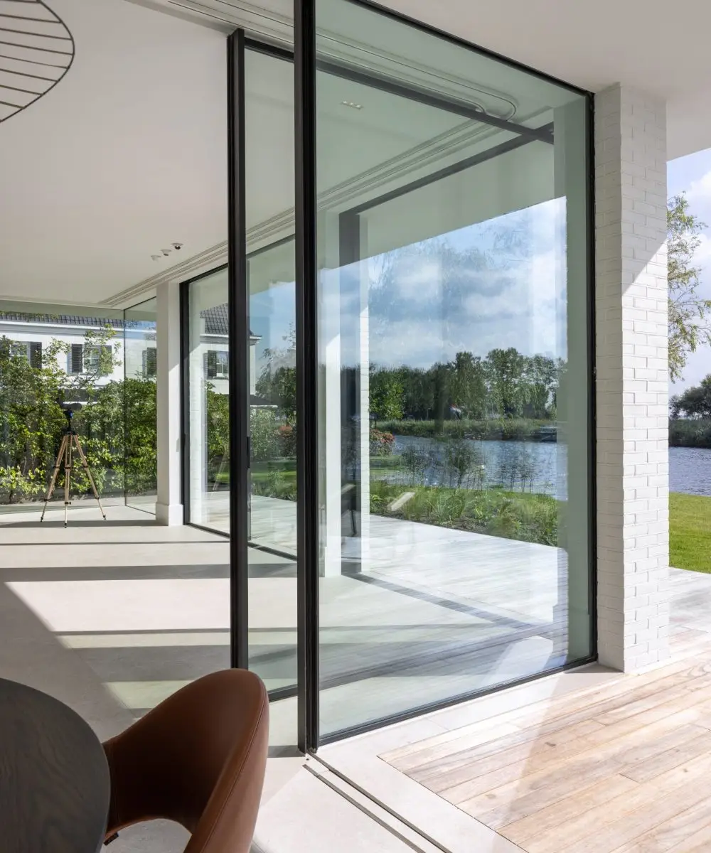 Moderne villa met glazen schuifpui en uitzicht op het water – interieur met naadloze overgang tussen binnen en buiten