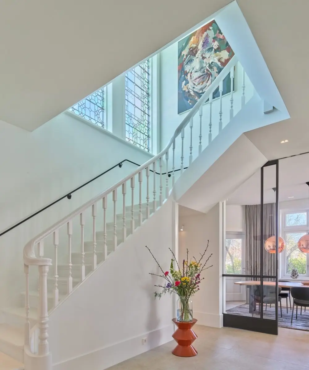 Lichtovergoten entree van gerenoveerde villa met klassieke trap, glas-in-lood ramen en zicht op de eetkamer