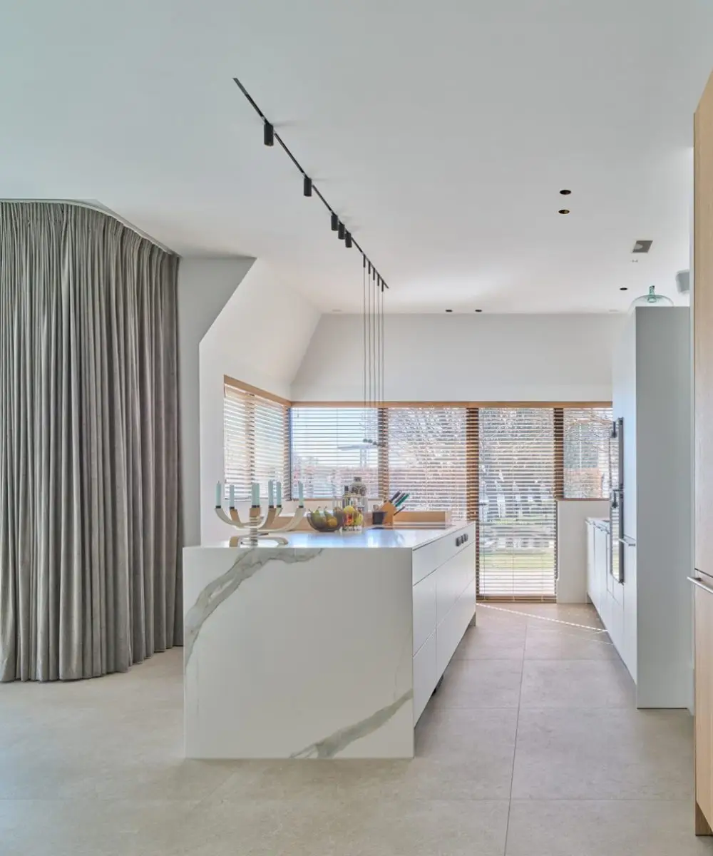 Luxe keuken met licht marmerlook kookeiland, grote ramen en moderne raambekleding – Villa aan de Leede