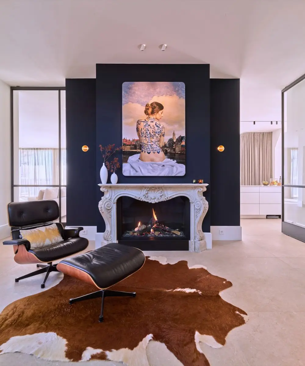 Entreehal met luxe haard, expressief schilderij en Eames Lounge Chair in villa aan het water