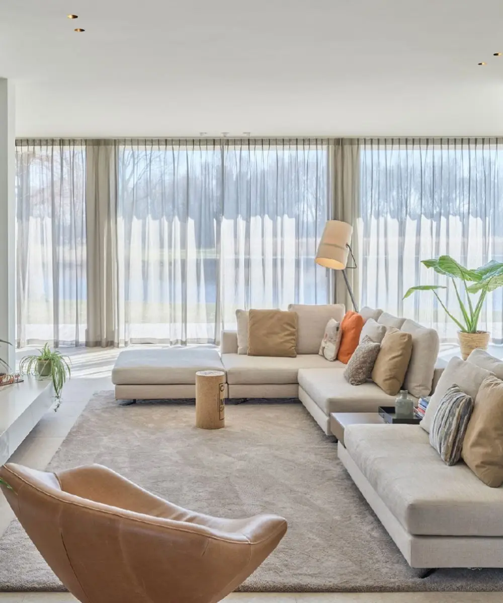 Lichte woonkamer met uitzicht op het water, moderne meubels en natuurlijke tinten – luxe villa verbouwing aan de Leede