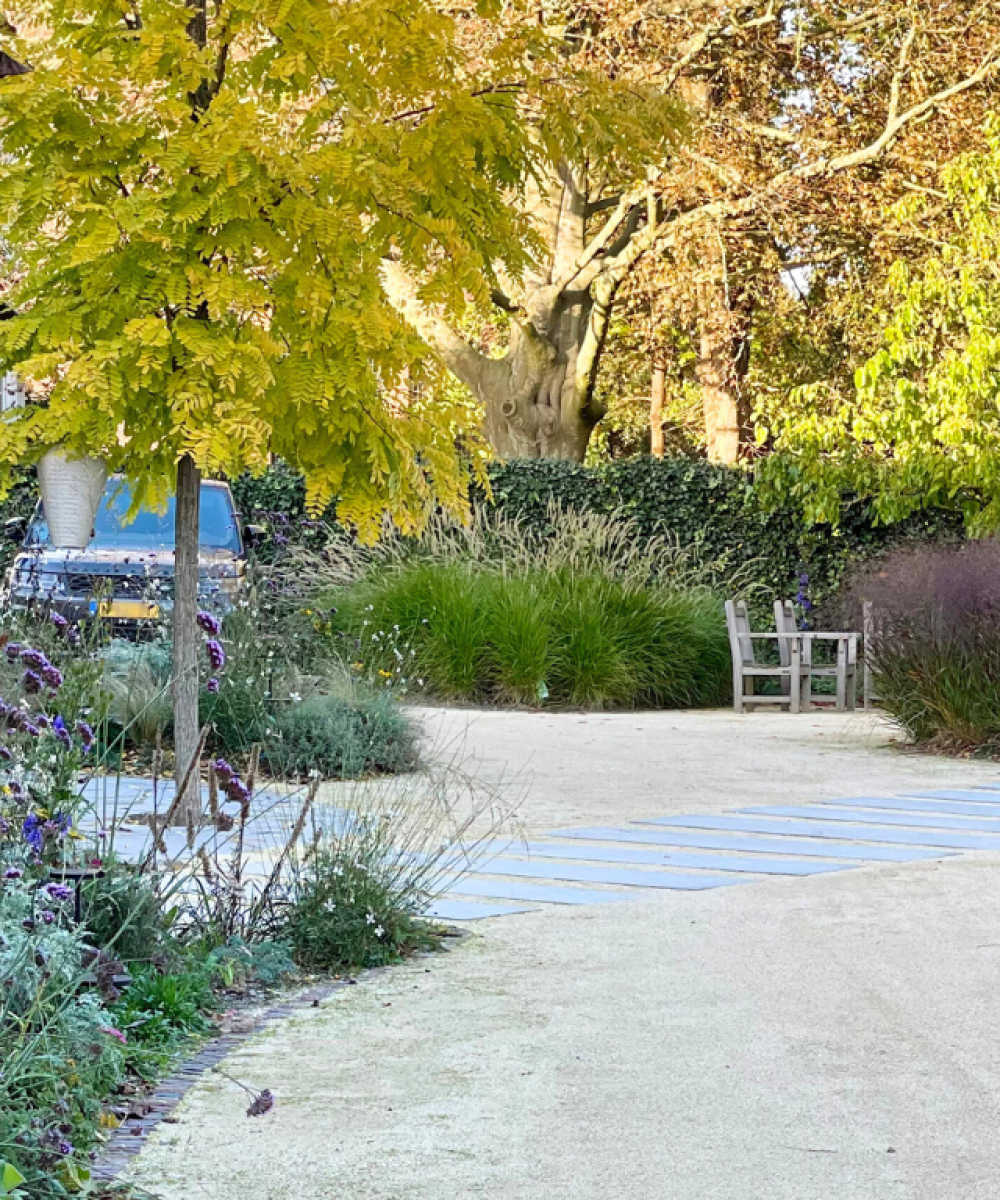 Halfverhard pad door de herfsttuin van Huize INA in Oegstgeest, met siergrassen, vaste planten en geel herfstblad