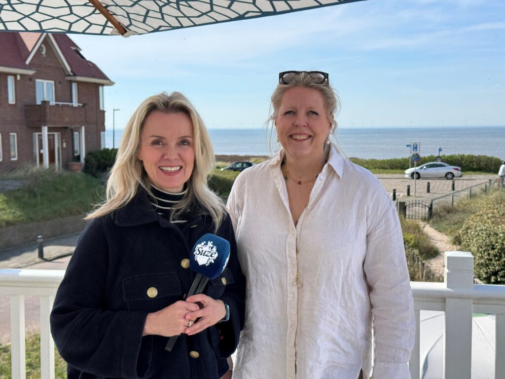 Ellis Kamerling en Suze Mens van Business Class op een terras met uitzicht op zee in Noordwijk aan Zee