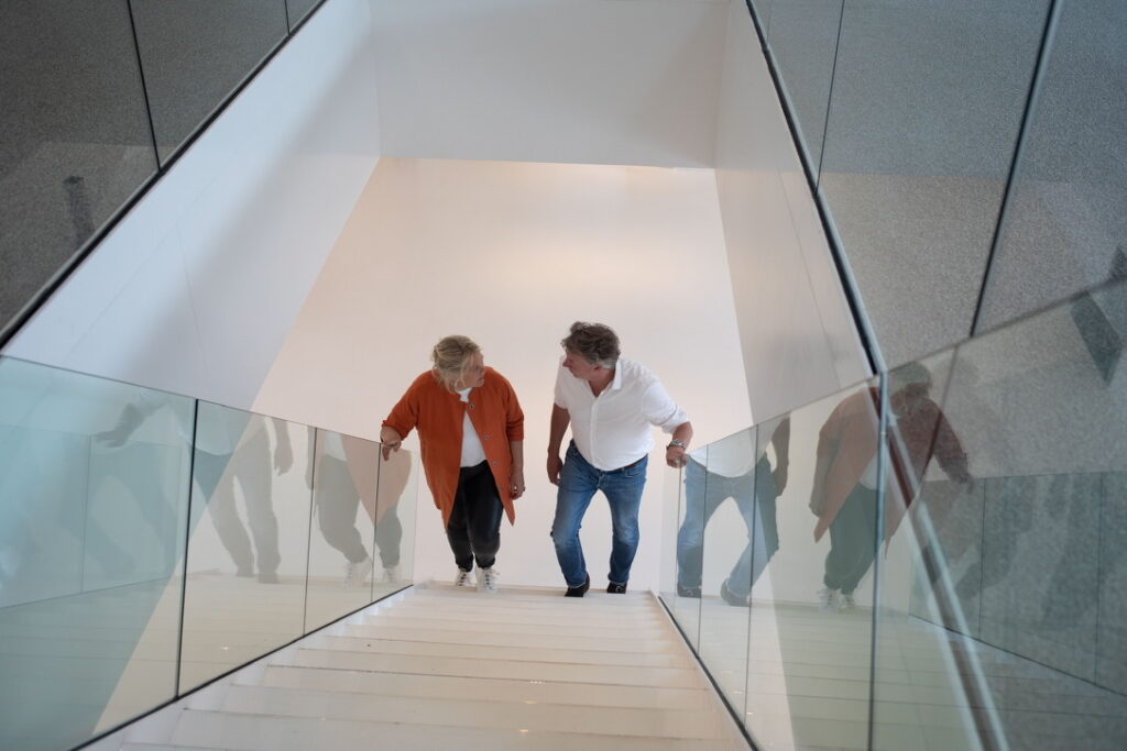 Ellis Kamerling en Cees van der Burgh lopen samen een witte trap met glazen balustrades op