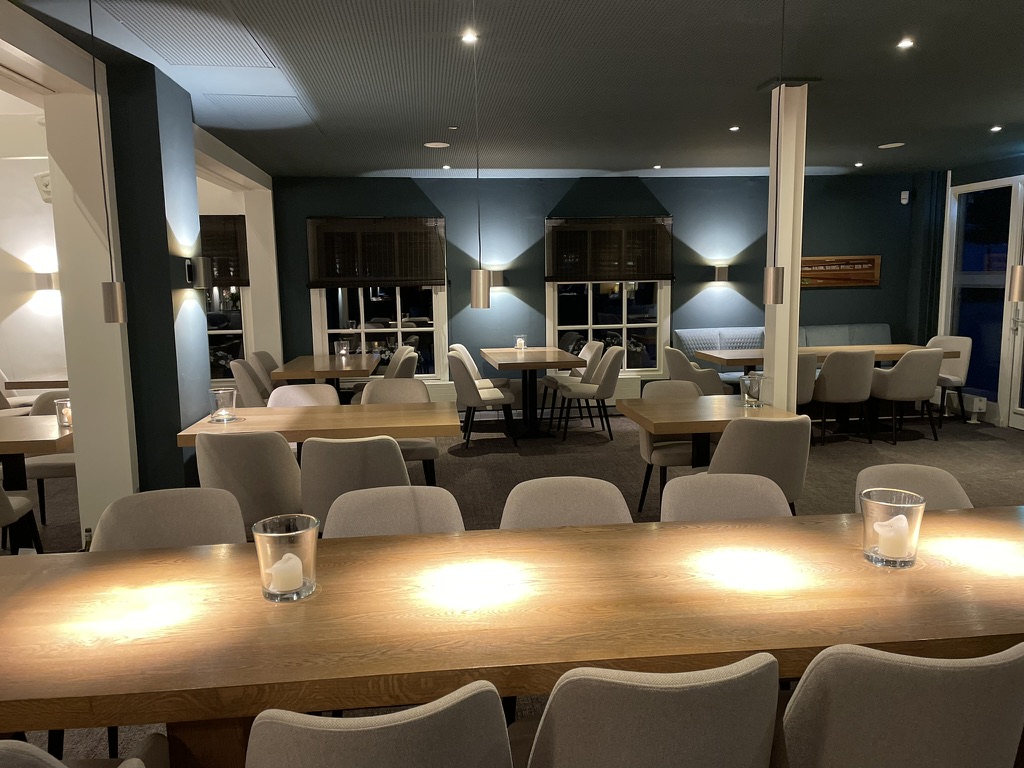 Restaurant in het clubhuis van Golfclub Rozenstein in Wassenaar na de verbouwing, met donkerblauwe wanden, lichte stoelen en een lange houten tafel
