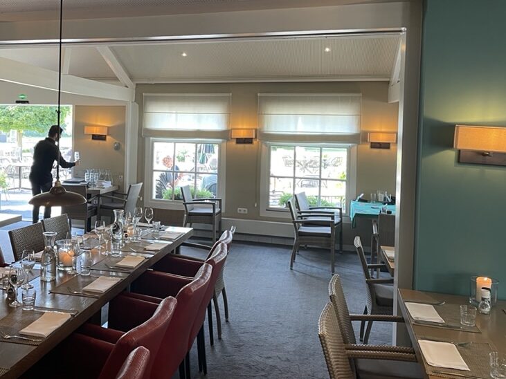 Restaurant in het clubhuis van Golfclub Rozenstein in Wassenaar voor de verbouwing, met een lange tafel, rode stoelen en groene kolommen