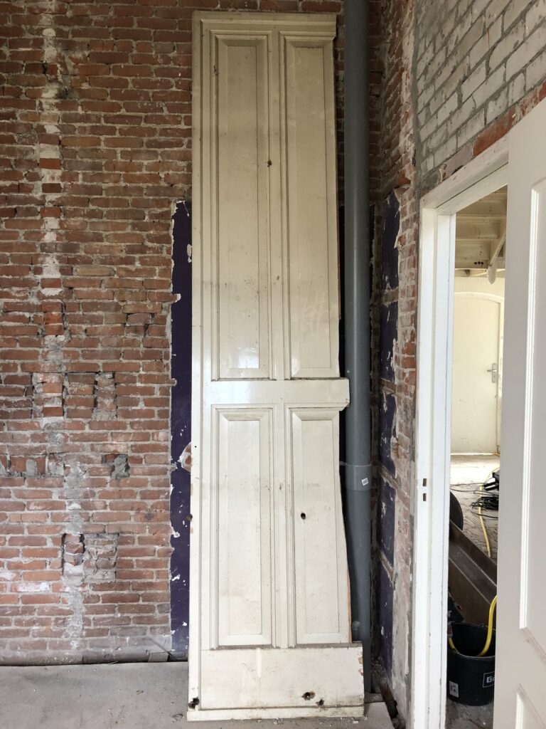 Originele paneeldeur tegen de kale bakstenen muur tijdens de verbouwing