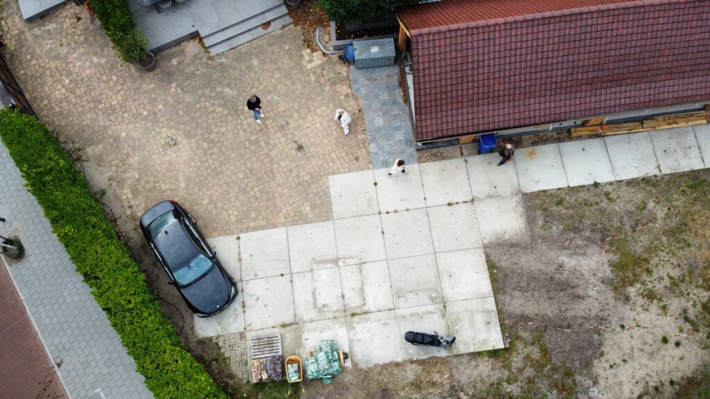 Luchtfoto van de bestaande situatie: betontegels, zand en de inrit naar de garage