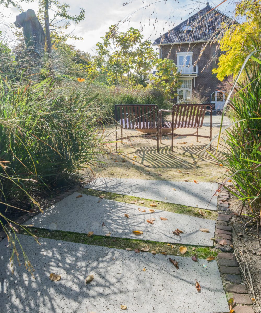 Brede betonplaten in een grafisch ritme tussen hoge siergrassen in de tuin van Huize INA, Oegstgeest