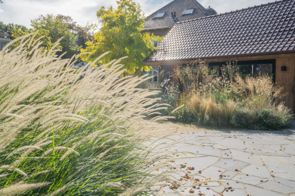 Het houten bijgebouw met garage en buitenkeuken in de tuin van Huize INA in Oegstgeest, met glas, siergrassen en een keerpunt van natuursteen