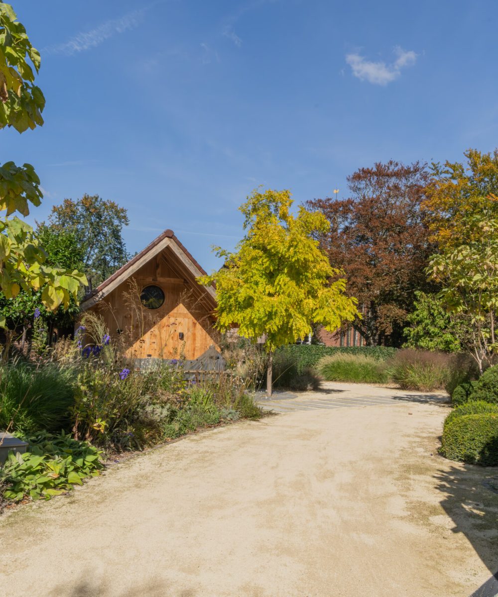 Pad van goudgele halfverharding door de beplanting naar het houten bijgebouw in de tuin van Huize INA, Oegstgeest