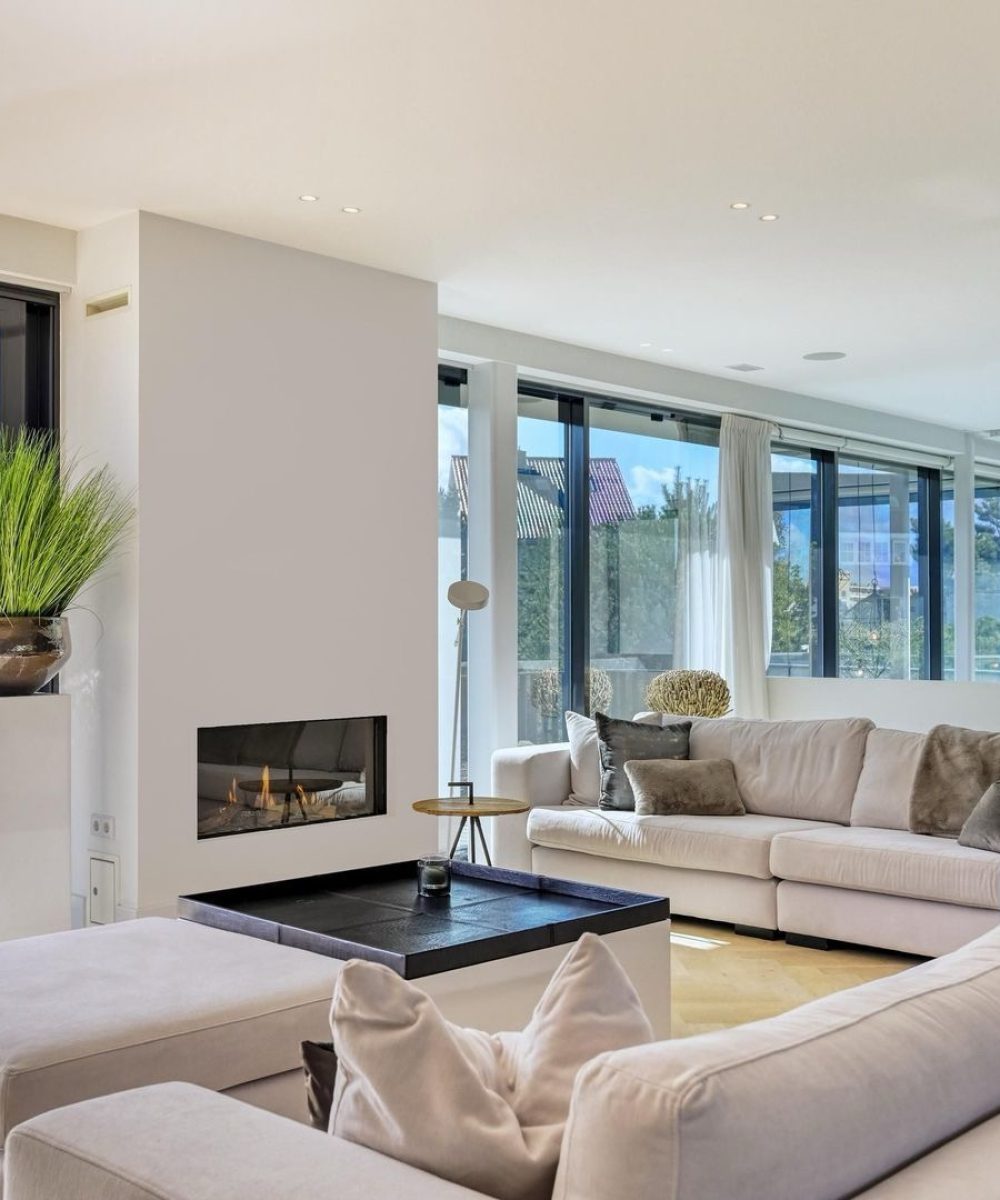 Woonkamer met haard en glazen pui in Villa Zuidduinen in Noordwijk. Ontwerp KamerlingvanderBurgh.